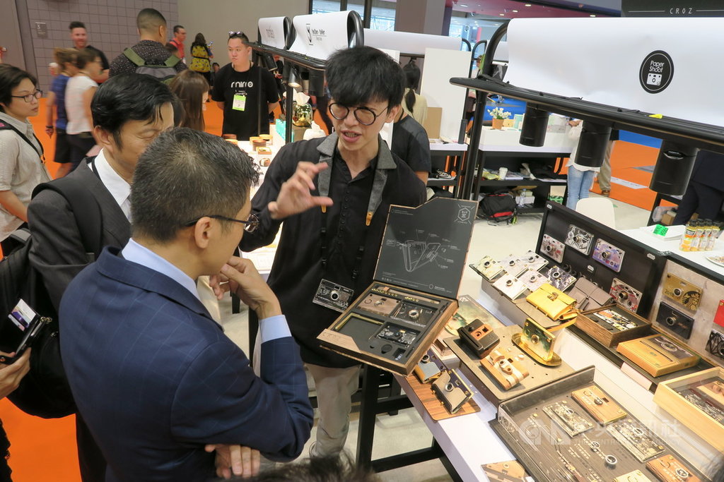 2019紐約禮品展夏季展11日登場,紙可拍PAPER SHOOT主打外殼多變的紙相機,紙綸科技公司創辦人林秋吉(右)向參觀者解說產品。中央社記者尹俊傑紐約攝 108年8月12日