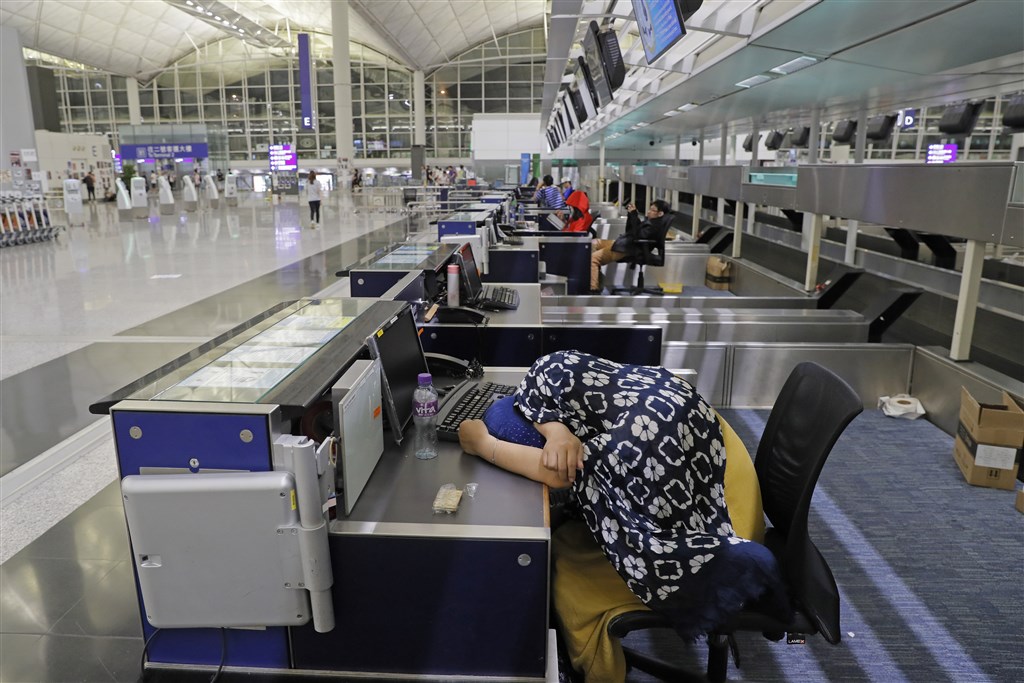 香港機場12日下午近4時宣布取消所有航班,滯留機場的旅客在航空公司報到櫃台睡覺或休息。(美聯社)