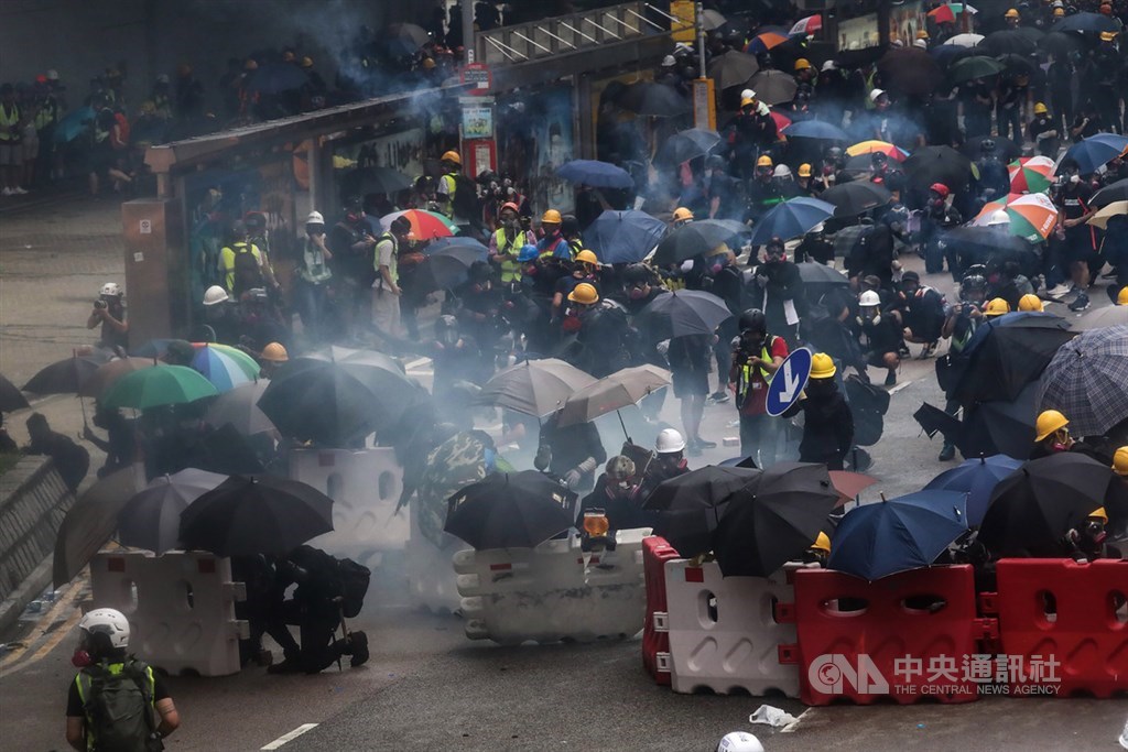香港網民31日發起「為香港罪人祈禱」反送中遊行,隨後大批群眾聚集在當地政府總部外,警方約在傍晚開始發射催淚彈驅離,現場示威者撐起傘,在路障拒馬旁蹲低身軀伺機應變。中央社記者吳家昇香港攝 108年8月31日