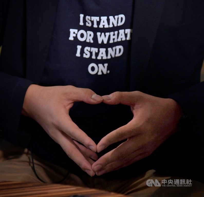 香港眾志秘書長黃之鋒5日在台北接受中央社專訪,他所穿T恤上的文字表達立場,雙手不經意擺出心型。中央社記者王飛華攝 108年9月5日
