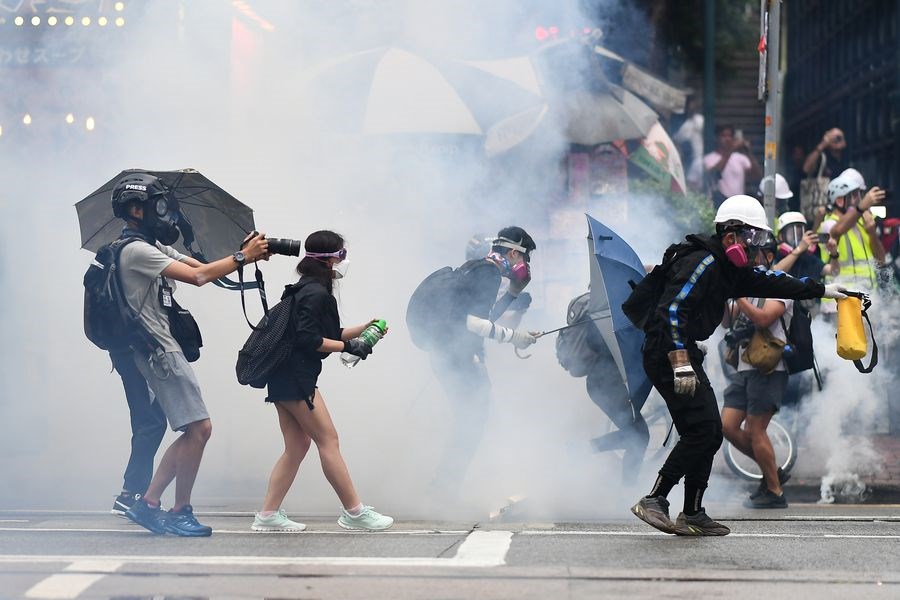 反對「禁蒙面法」的示威者10月6日下午冒雨兵分多路上街,警方發射催淚彈清場,示威者撐起傘陣掩護撤離。(法新社提供)