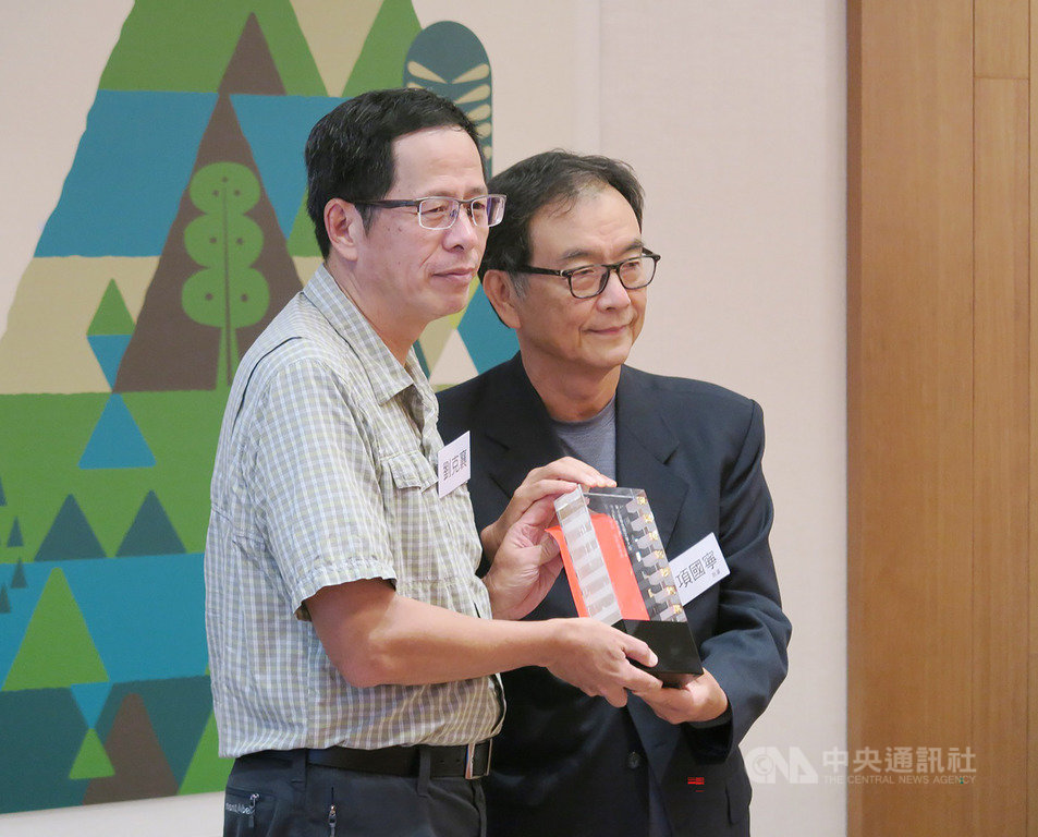 2019第6屆聯合報文學大獎贈獎典禮6日在台北舉行,本屆獲獎作家劉克襄(左)親自出席,從聯合報執行董事項國寧(右)手中接下獎座。劉克襄說,獲獎是提示他不要迷路,要重新再與這片土地對話。中央社記者陳政偉攝 108年10月6日