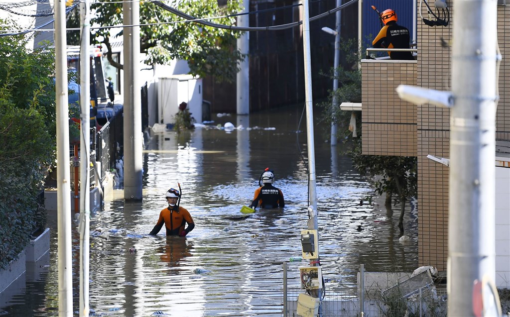 夾帶強烈風雨而來的颱風哈吉貝導致日本多處下起紀錄性大雨。圖為13日上午川崎市淹水,消防員涉水善後。(共同社提供)
