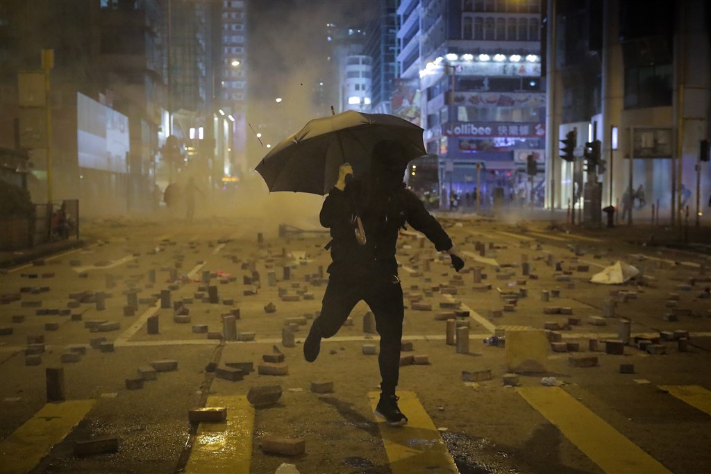 香港「三罷」運動在入夜後,示威者轉回中環、旺角、銅鑼灣與西灣河等地,在街道築起路障、焚燒雜物與噴寫抗議標語。圖為一名示威者逃離港警發射的催淚彈。(美聯社)