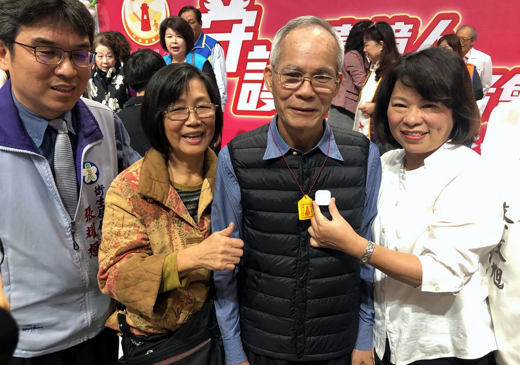 嘉義市衛生局為預防失智長輩走失,製作輕巧的防走失載具,同時利用長輩的宗教信仰,包括可裝置載具的平安符、十字架小皮夾或福袋送給長輩,讓他們願意攜帶。市長黃敏惠(右)9日為長者佩帶。中央社記者黃國芳攝 108年12月9日