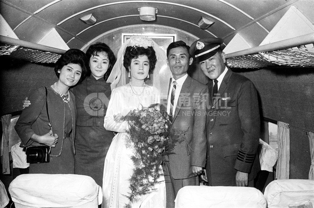 一對青年男女於1965年自高雄搭乘遠航班機到台北途中,在機上舉行空中結婚典禮,遠航公司總機師毛昭宇(右)證婚,空服員郭儀(左2)擔任司儀,雙方親友多人在場觀禮。(中央社檔案照片)
