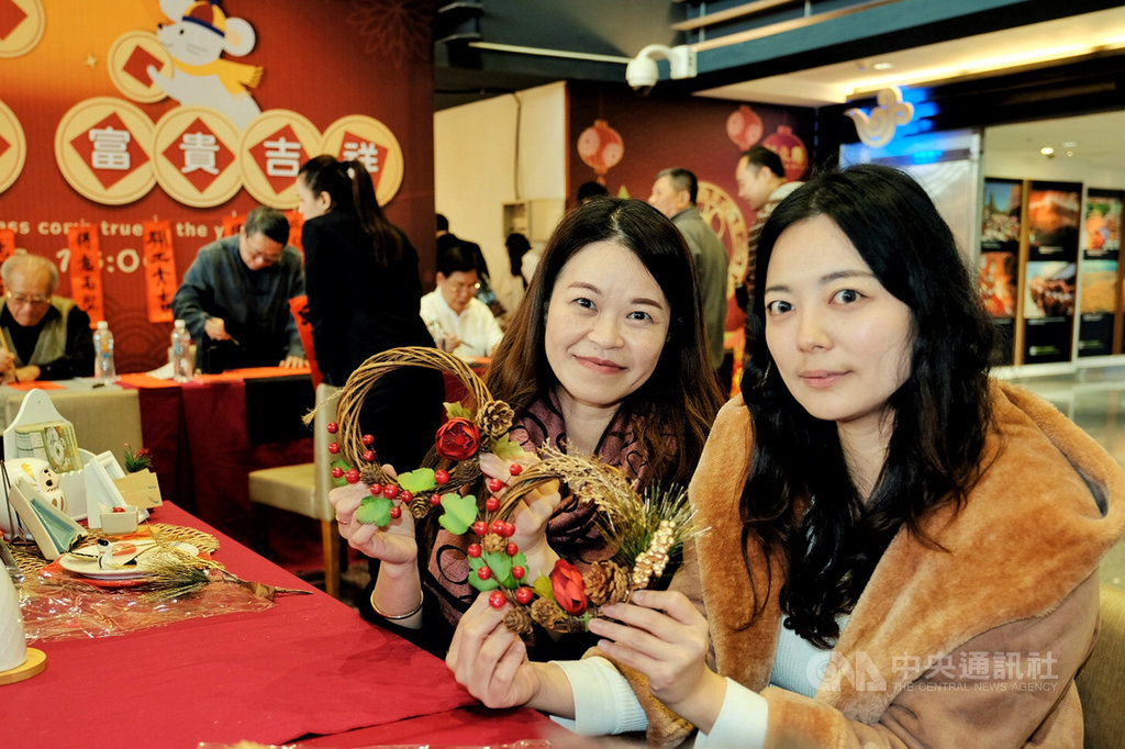 農曆春節將至,桃園國際機場第一航廈出境大廳14日下午不僅有書法家現場揮毫寫春聯分送旅客,還設置新春花圈的DIY活動攤位,工作人員指導旅客製作出屬於自己的新春花圈,造型小巧可愛還具有祈福之意。中央社記者吳睿騏桃園機場攝 109年1月14日