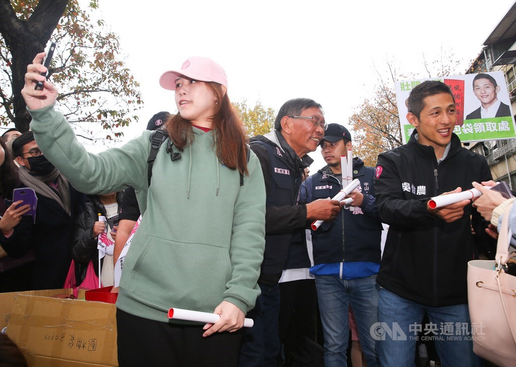 參選立委失利的民進黨候選人吳怡農(右)18日在台北市錦西街和民生西路70巷口發送春聯與紅包袋,除向選民表達謝意,也向民眾提早拜年,不少民眾拿著手機想與吳怡農同框合影。中央社記者謝佳璋攝 109年1月18日