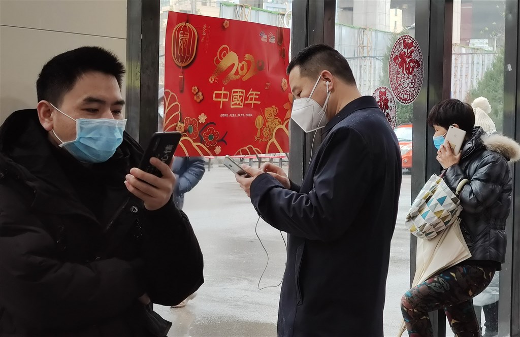 受武漢肺炎疫情影響,今年中國各大城市年味變調。圖為24日湖北省武漢市一商店外,民眾與外地員工以手機向親友報平安。(中新社提供)