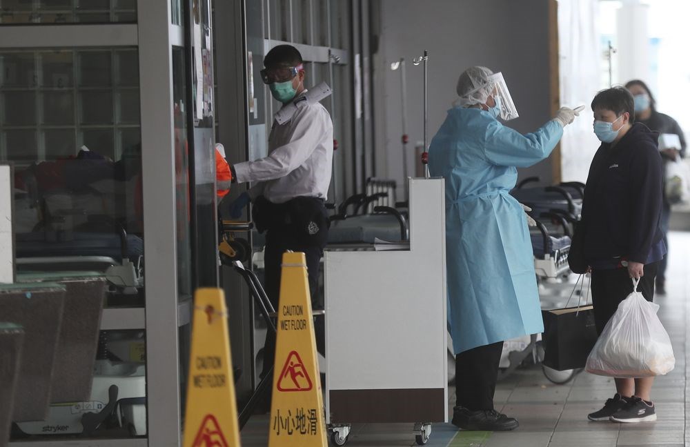 武漢肺炎持續擴散，香港9日新增3名確診病例，其中2例為一名24歲男病患，以及他的90歲祖母，他們家族成員中的另外7人初步確診感染武漢肺炎。圖為身穿防護衣的香港瑪嘉烈醫院人員檢測民眾體溫。（美聯社）
