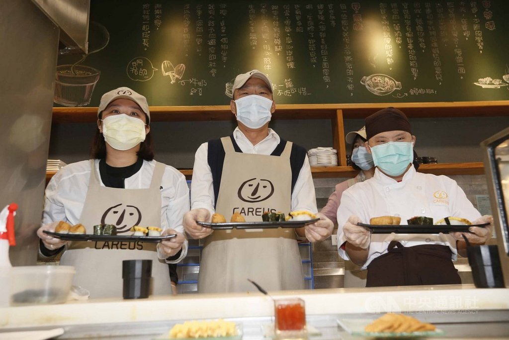 高雄市長韓國瑜(中)27日訪視喜憨兒創作料理庇護商店,與憨兒小維(右)學做握壽司,行銷庇護商店的特色餐飲。中央社記者董俊志攝 109年2月27日