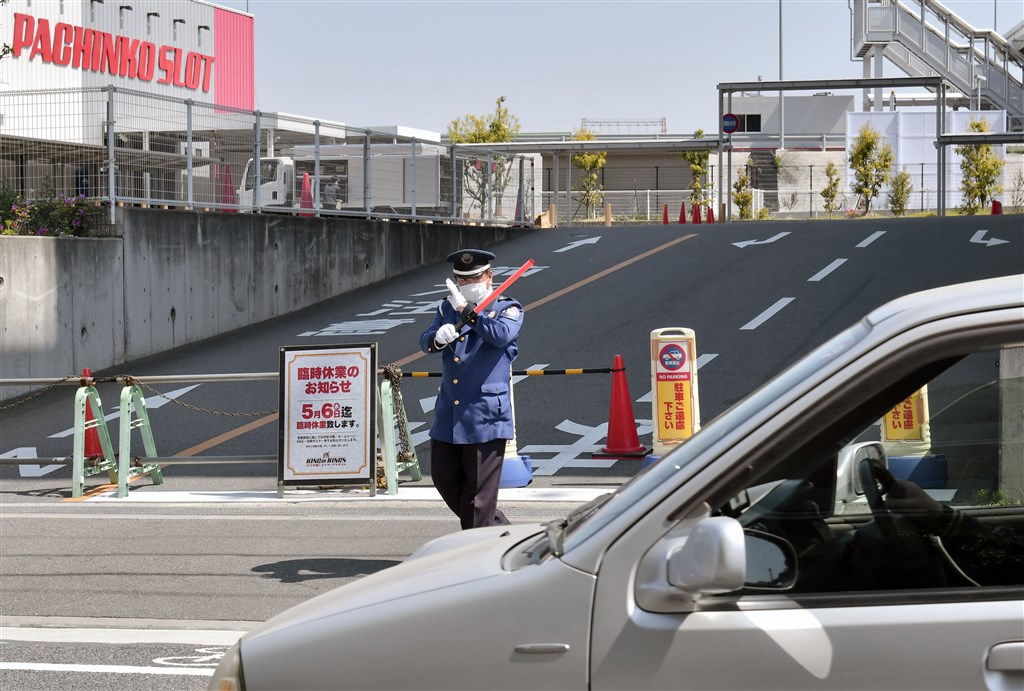 圖為大阪柏青哥業者臨時停業,出入口設立告示並由警衛人員引導民眾離場。(共同社提供)