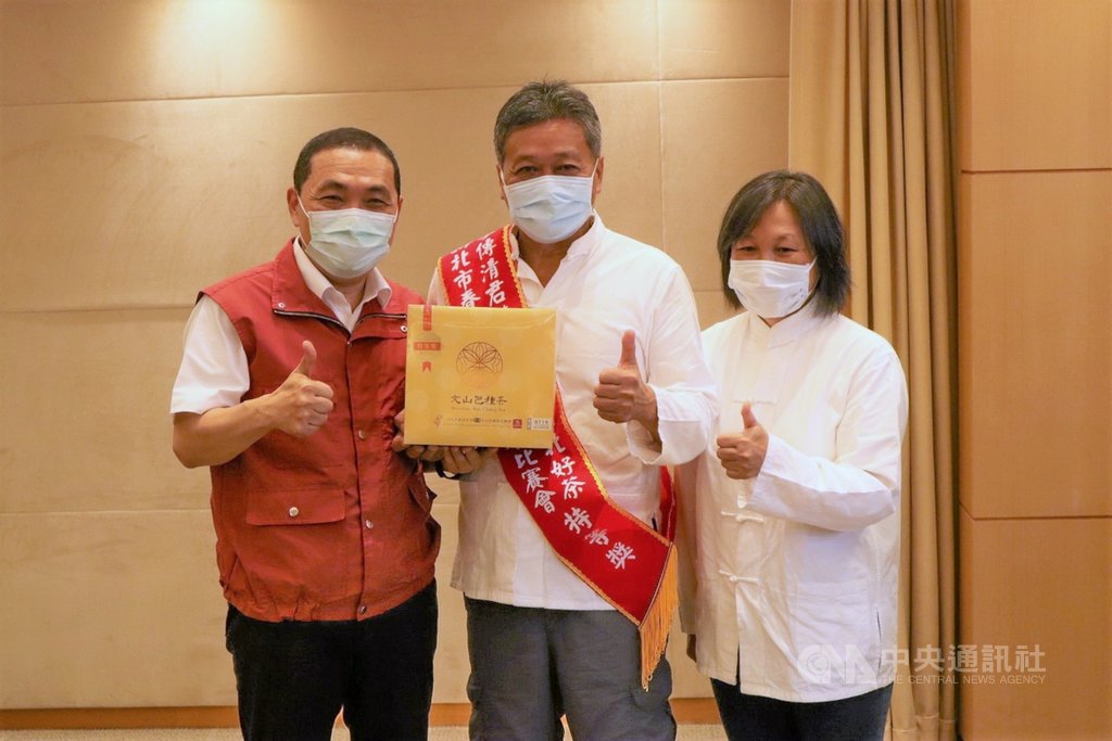 新北市坪林茶農李傳清(中)平時與妻子一起管理茶園,今年獲選「新北好茶春季包種茶」評鑑特等獎,3日接受市長侯友宜(左)頒發特等獎匾額鼓勵,李傳清也致贈茶葉給侯友宜。(農業局提供)中央社記者黃旭昇新北傳真 109年6月3日