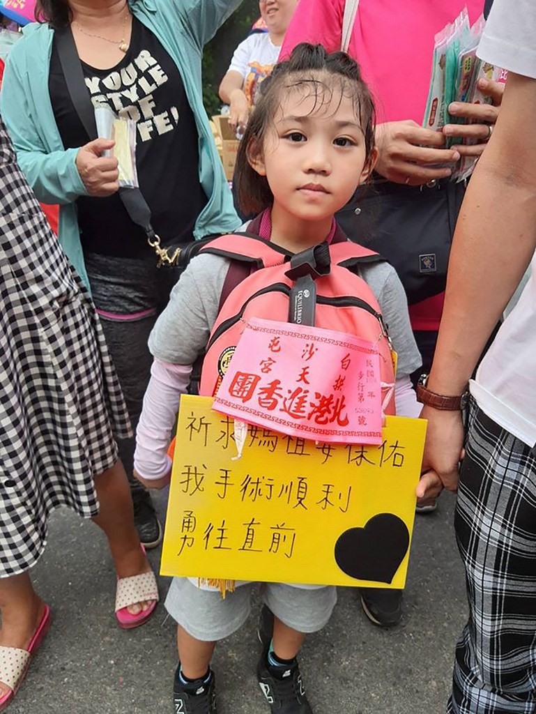 白沙屯媽祖徒步進香之旅,7日上午從彰化縣進入雲林縣境內,有眼尖香客發現隊伍中有名年僅6歲的羅小妹妹(圖)由舅舅王志剛牽著步行,她的身上揹著牌子寫著「祈求媽祖要保佑我手術順利,勇往直前」,為10日將進行的第4次手術祈福。(民眾提供) 中央社記者姜宜菁傳真 109年7月7日
