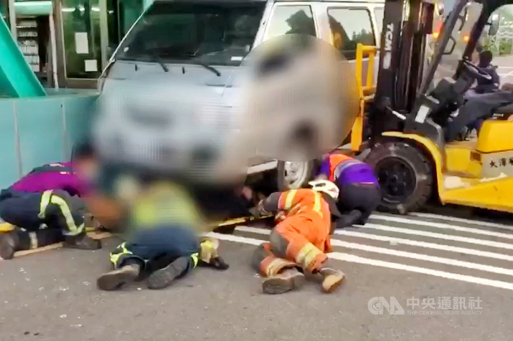 桃園市觀音區大潭電廠警衛室旁2名保全人員9日遭廂型車撞上並卡在車底,救護人員立即找來堆高機抬高廂型車,將2人從車底拉出送醫,其中一人送醫後宣告不治,另一名男子目前住院觀察中。(桃園市政府消防局提供)中央社記者吳睿騏桃園傳真 109年7月10日