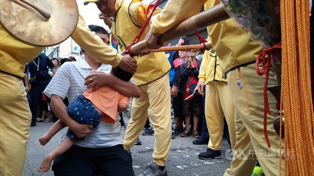 白沙屯媽祖回鑾11日抵台中,經過沙鹿區鹿寮成衣商圈時,一名服飾店業者抱著2歲大的孫子跪在神轎前,盼媽祖為生病的孩子賜福,神轎則不斷在祖孫2人旁擺動,讓信徒們相當感動。(民眾提供)中央社記者蘇木春傳真 109年7月11日