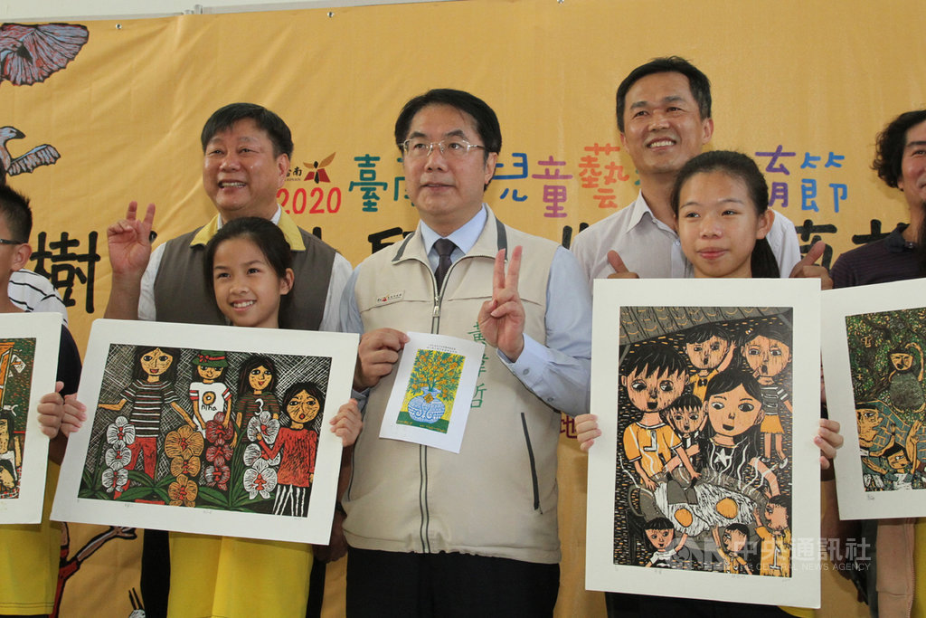 台南市長黃偉哲(前中)13日出席在中西區南美里活動中心舉辦的樹人國小師生版畫特展開幕儀式,拿著自己在現場體驗創作的版畫作品與參展學生合照。中央社記者楊思瑞攝 109年7月13日