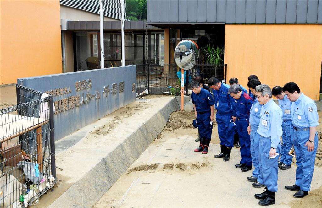 日本許多地區過去一週受豪雨重創,首相安倍晉三(右4)13日上午搭機前往災區的老人中心「千壽園」探視,站在目前仍殘留泥巴及瓦礫的設施前,為罹難者默禱。(共同社提供)