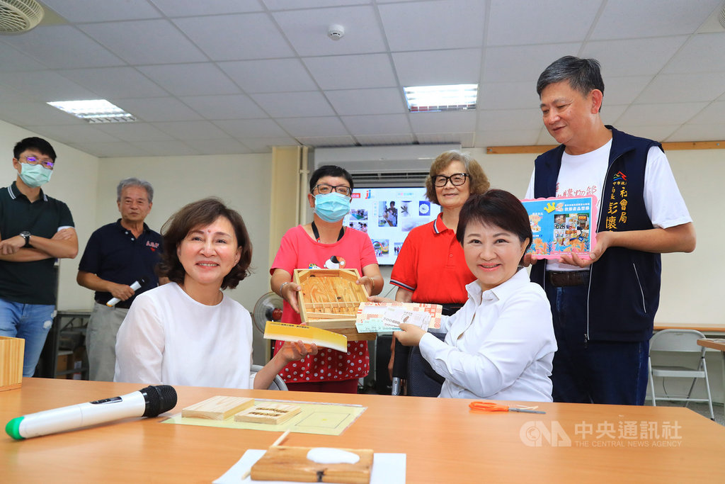 台中市長盧秀燕(前右)術後行動仍不便,30日坐著輪椅到環保木工坊「新窩工坊」,持振興三倍券購買學員手工打造的木製彈珠台,將轉贈台中9間親子館,做為小朋友的遊戲玩具。中央社記者郝雪卿攝 109年7月30日