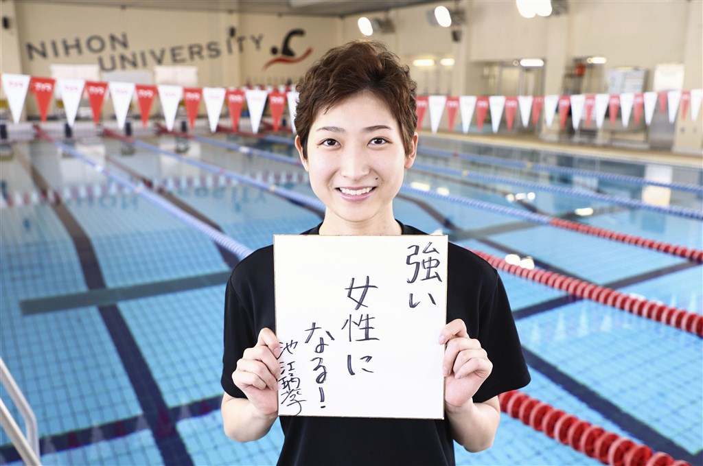 日本明星泳將池江璃花子去年2月被診斷出罹患白血病,經過一年多治療和恢復訓練後,她7月23日出席公開練習並拿著勵志標語。(共同社)