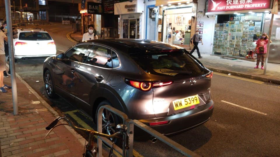 香港泛民派立法會議員許智峯(站立車前白衣人)14日晚間攔下一輛跟蹤他的深灰色自小客車,欲追問跟蹤人士身分。(取自許智峯臉書)中央社 109年8月15日