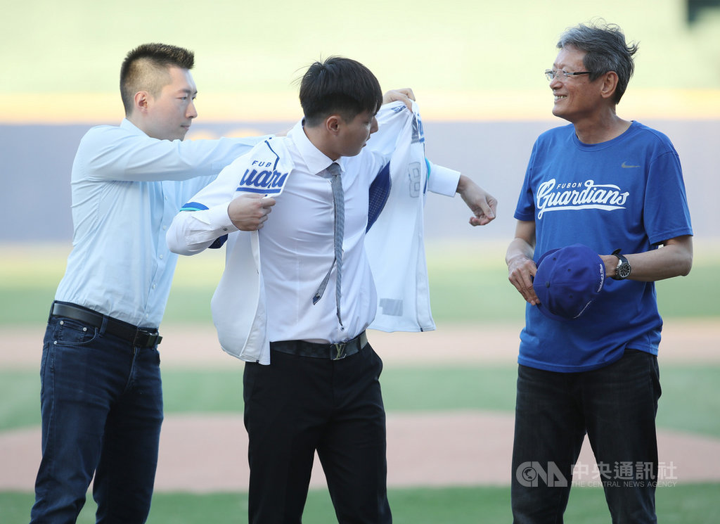 中職富邦悍將今年季中選秀第二輪選進旅日好手郭俊麟(中),1日在新莊球場舉辦加盟儀式,領隊蔡承儒(左)為他穿上球衣,顧問郭泰源(右)為他戴上帽子。中央社記者張新偉攝 109年10月1日