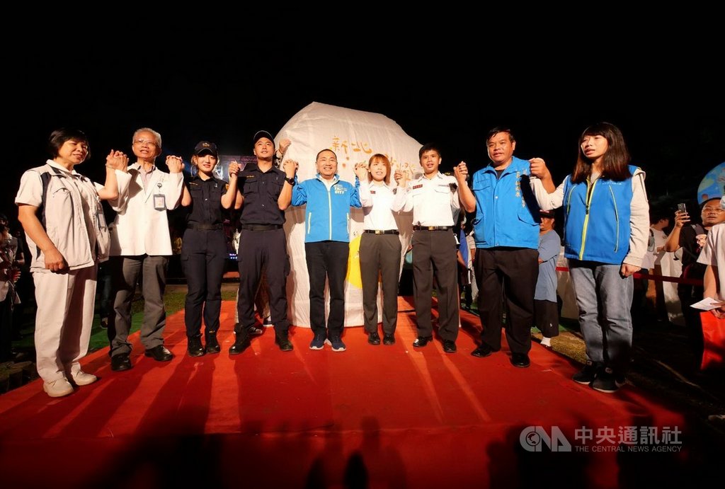 「新北點燈.向世界報平安」活動1日晚間在平溪登場,新北市長侯友宜(左5)在舞台上牽起警察、消防、衛生等防疫夥伴的手致敬,並一起題字與放天燈。(新北觀旅局提供)中央社記者黃旭昇新北傳真 109年10月1日