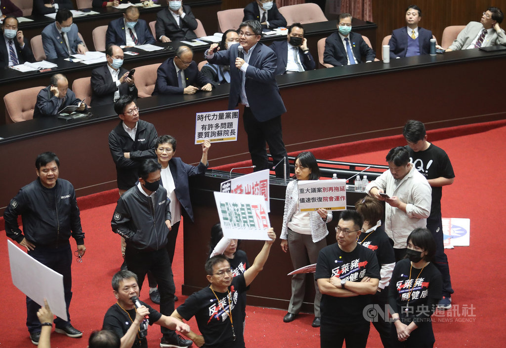 行政院長蘇貞昌27日第13度赴立法院進行施政報告並備質詢,時代力量邱顯智(拿麥克風者)質詢時,受到國民黨立委拿紙板阻擋與哨音干擾,便站到椅子上發言。前右2為國民黨主席江啟臣。中央社記者張新偉攝 109年11月27日