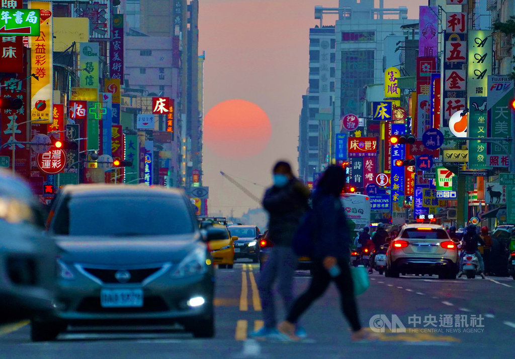 高雄市青年路「懸日」美景28日傍晚再度現身,橘澄澄的太陽緩緩落下,以車水馬龍的街道與五光十色的招牌為襯,格外吸睛,也吸引許多攝影愛好者前往搶拍。中央社記者董俊志攝 110年1月28日