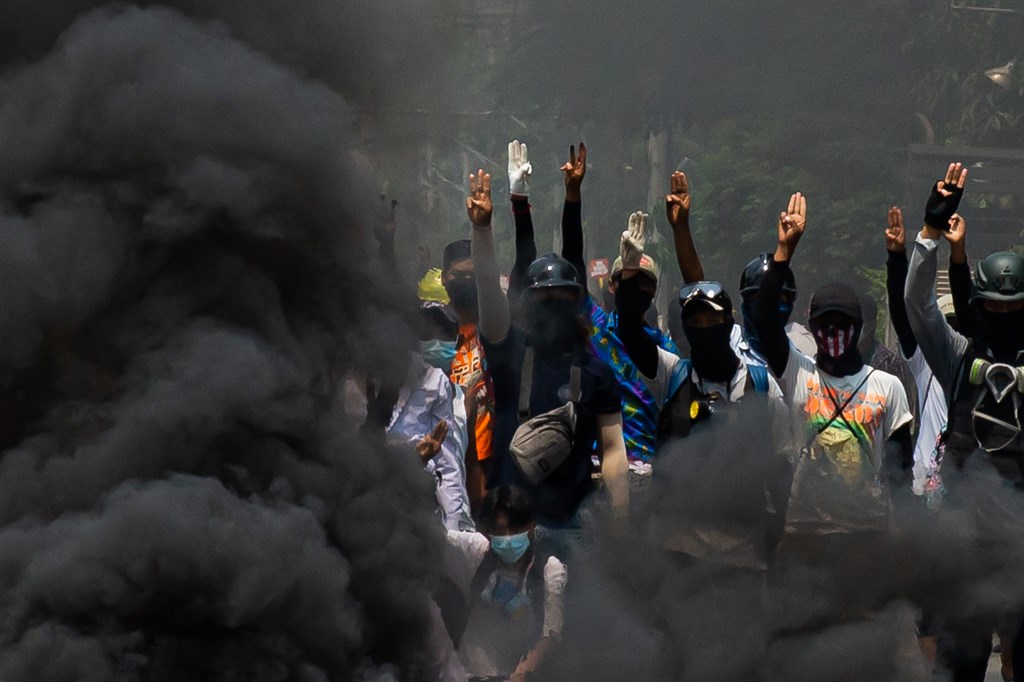緬甸安全部隊27日殘暴鎮壓爭取民主的示威抗議者，在全國各地總共殺害114人，包括若干小孩在內。圖為27日仰光街頭示威民眾在燃燒輪胎的煙霧中高舉三指手勢。（安納杜魯新聞社）