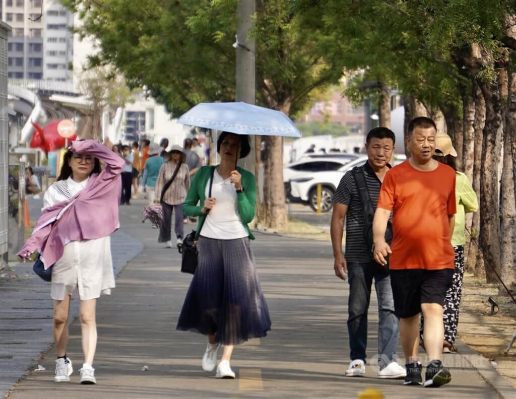 圖為高雄駁二藝術特區周邊民眾撐傘、舉起手遮擋豔陽。（圖／中央社）