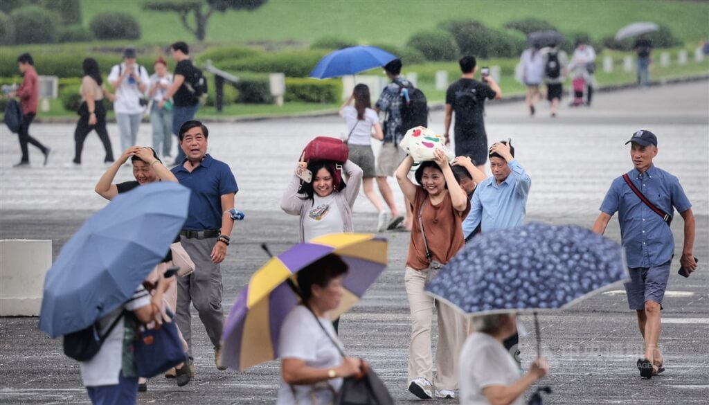 台北自由廣場遊客午後遇雨，未備雨具的民眾高舉包包或以手遮擋雨勢。（圖／中央社）