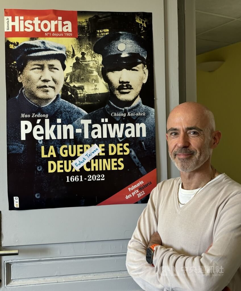 長期推動法國認識台灣的學者高格孚接受中央社專訪，分析聯大2758號決議歷史背景及其荒謬之處。後方海報為高格孚主編法國百年歷史雜誌Historia的台灣封面故事， ​​​​​​​邀請多位學者從南島語族原住民開始講述台灣史。（圖／中央社）