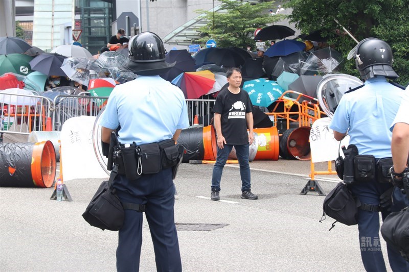 香港12日再度爆發反對逃犯修例的示威。民主黨主席胡志偉(正面著黑衣者)站在被示威者占領的夏愨道西端,帶頭與警方對峙。中央社記者張謙香港攝 108年6月12日