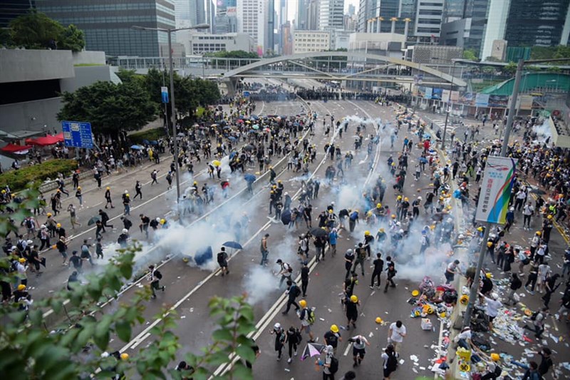 香港警察12日對「反送中」抗議展開清場,動用催淚彈,導致許多抗議民眾奔逃,但也有人上前用雨傘防止濃煙擴散,再使用礦泉水試圖稀釋煙霧。中央社記者侯文婷攝 108年6月12日