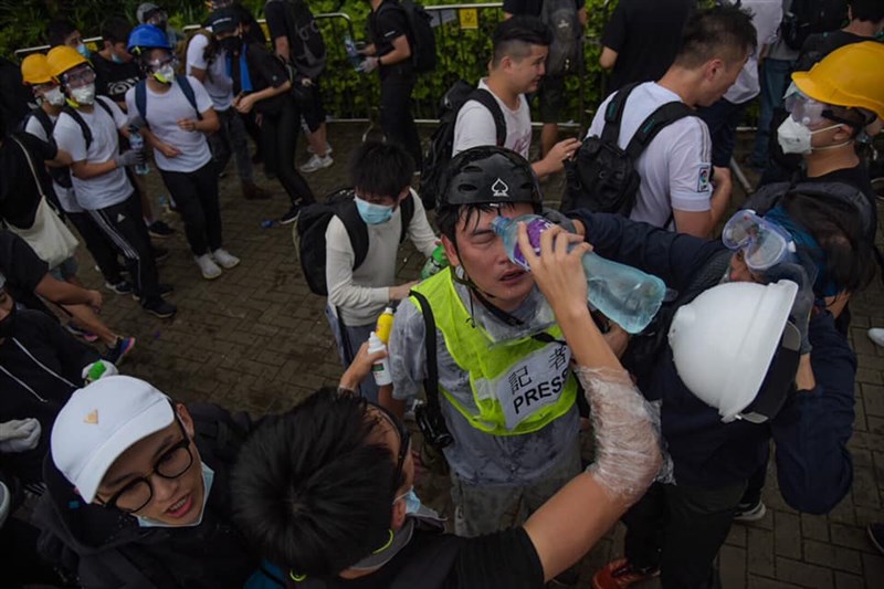 香港「反送中」抗議民眾12日試圖衝入立法會,警方使用催淚彈嚇阻,現場記者也受到波及,一旁有人使用礦泉水協助,試圖減緩嗆辣濃煙造成的刺痛感。中央社記者侯文婷攝 108年6月12日