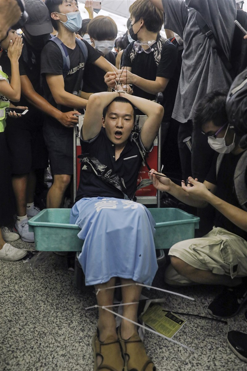 反送中示威者13日持續在香港機場集會,環球時報記者付國豪(前中)被示威者用索帶綁在機場行李車上。(美聯社)