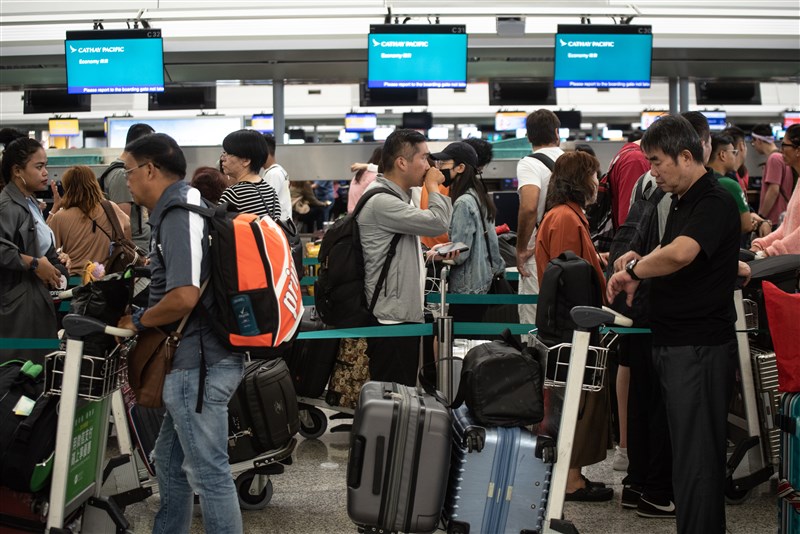 香港機場14日恢復運作,班機上午大多按照預定時間離境。圖為乘客在航空公司報到櫃台前排隊等候。(法新社提供)