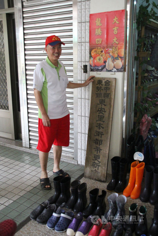 九二一地震毀了東勢本街,也意外讓林宗立從鞋店老闆轉身變成社區重建工作者。圖為林宗立在當年都更的牌子前合影。中央社記者林克倫攝 108年9月19日