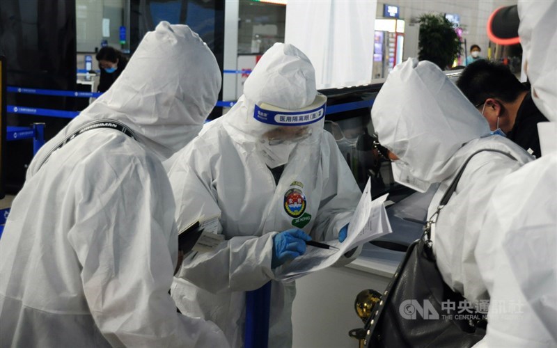 兩名搭乘20日晚間類包機的國人穿上自備的防護衣,和上海機場防疫人員(中)核對資料。中央社記者沈朋達上海攝 109年4月20日