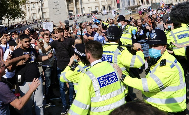 為因應武漢肺炎病例激增,英國19日宣布嚴格新規定,民眾如果拒絕自我隔離以遏止病毒擴散,最高可處1萬英鎊(約新台幣38.7萬元)重罰。圖為倫敦民眾抗疫防疫措施與警方對峙。(安納杜魯新聞社)