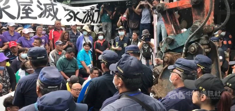 屏東縣政府15日出動怪手強制拆除瑪家鄉禮納里永久屋的2棟大型違建，屋主之一的霧台鄉鄉代李金龍帶領族人在違建前靜坐，警方也出動大批人力維持秩序。中央社記者郭芷瑄攝 109年10月15日