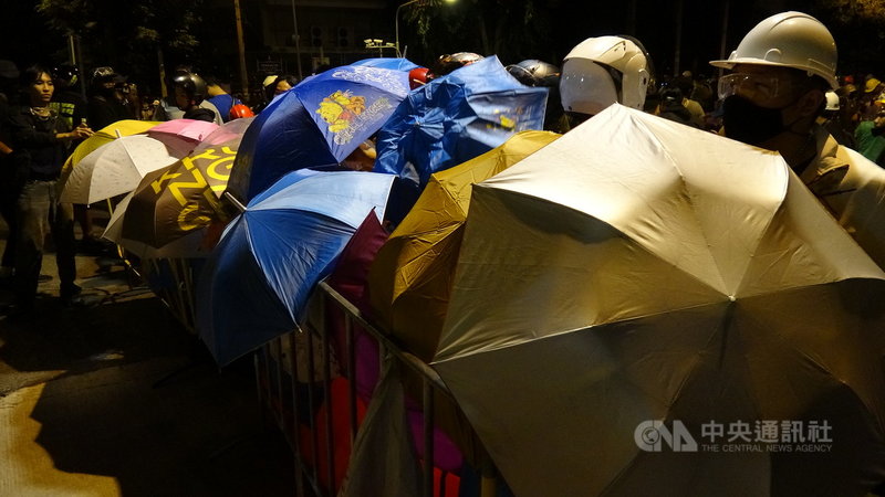 泰國民眾21日下午無預警遊行到總理府前要總理帕拉育下台,由於擔心警方再度出動水柱驅離,抗議民眾撐起雨傘備戰。中央社記者呂欣憓曼谷攝 109年10月21日