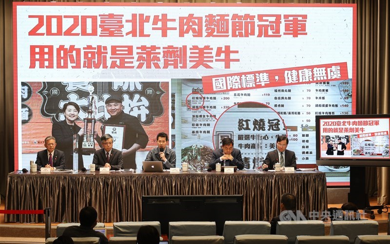 行政院發言人丁怡銘(後中)12日主持行政院會後記者會,會中秀圖表示,台北市辦的牛肉麵節,今年冠軍用的就是含有萊克多巴胺的美牛,證明只要符合聯合國食安標準,安全不會有問題。如果萊克多巴胺有問題,台北市不會由副市長親自頒獎。中央社記者謝佳璋攝 109年11月12日