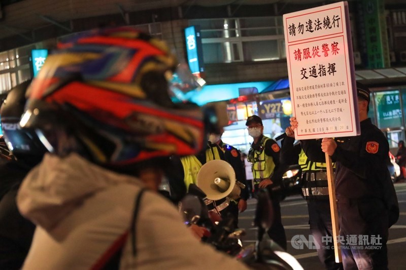 民間團體20日為抗議塔城街與鄭州路口強制機車兩段式左轉政策,發起「待轉大富翁–全員四輪大迷航」活動,警方派員到場,舉牌提醒騎士勿違法繞行。中央社記者吳家昇攝 109年11月20日