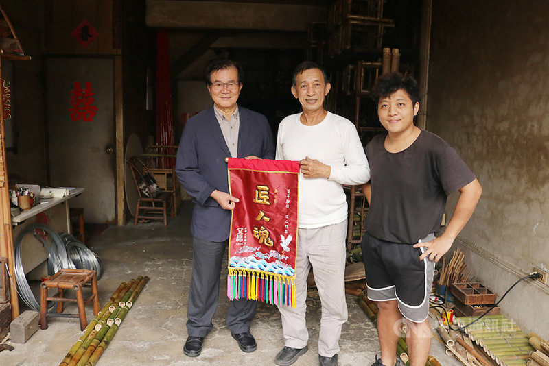 中華文化總會「匠人魂」系列影片拍攝台南府城碩果僅存的竹業工藝百年老店「信二竹店」,記錄傳承4代的匠人精神;文總副會長江春男(左)日前贈與現任負責人王壬煇(中)一面匠人魂錦旗,並向他致敬。(文總提供)中央社記者鄭景雯傳真 109年12月18日