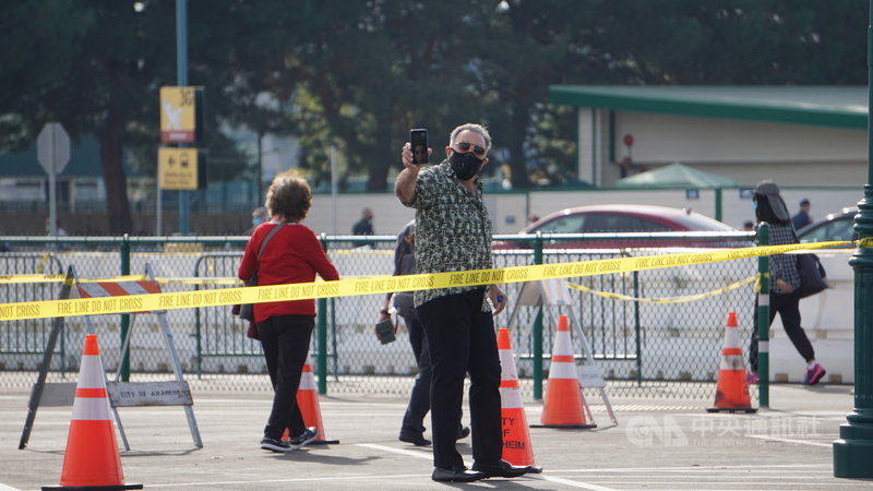 加州橘郡與迪士尼樂園合作,13日起在停車場設置大型疫苗注射中心。圖為前來施打疫苗的民眾行經記者會場拿出手機拍照。中央社記者林宏翰洛杉磯攝 110年1月14日