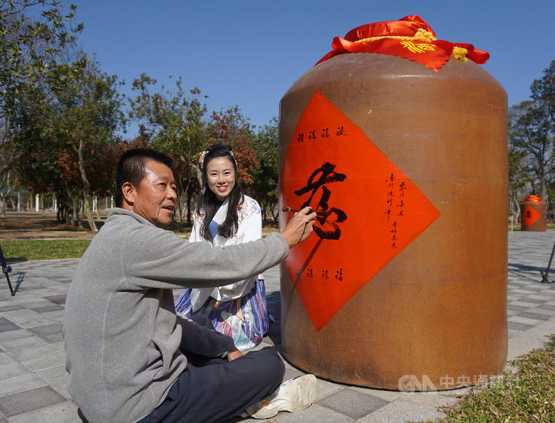 金門縣林務所與金酒公司合作,利用淘汰的60個1000公升大酒甕,套上紅布並邀請書法老師現場揮毫,前縣長李炷烽(左)也共襄盛舉,為林務所年度假日花市活動增添藝文氣息。中央社記者黃慧敏攝 110年1月30日