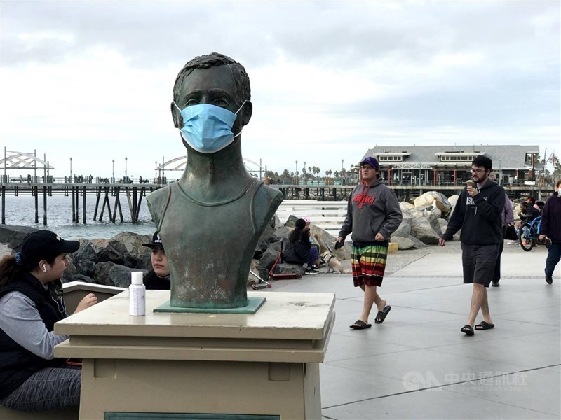 美國南加州芮當多海灘傳奇救生員佛利斯雕像戴上口罩,與周圍不戴口罩的遊客形成對比。(中央社檔案照片)