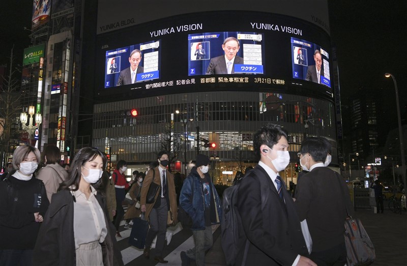 日本在野黨認為，導致疫情再度擴大的主因包括日本政府解除「緊急事態宣言」的時機過早。圖為3月18日晚間東京街頭電視牆播放首相菅義偉宣布解除緊急事態宣言的新聞畫面。（共同社）